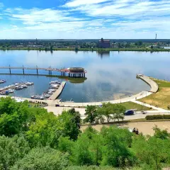 Płock co zobaczyć: malownicza marina z żaglówkami, nowoczesny deptak nad Wisłą i industrialne krajobrazy w tle.