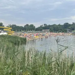 Tłum ludzi wypoczywa nad wodą na plaży w Lisowicach. W oddali widać żółtą zjeżdżalnię wodną.