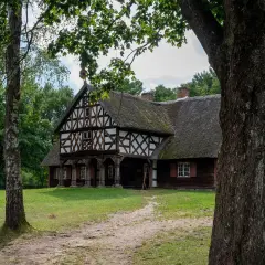 Drewniany dom z muru pruskiego i strzechą, otoczony zielenią. Jedna z atrakcji Olsztynka, zapraszająca do podróży w czasie.