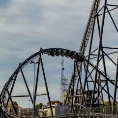 Pasażerowie jadą najwyższym rollercoasterem w Europie, który pędzi po stalowych torach na tle błękitnego nieba.