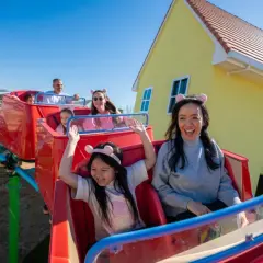 Rodzina cieszy się przejażdżką w Peppa Land Polska, z uśmiechniętymi dziećmi w uszkach świnki.