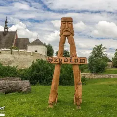 Drewniana rzeźba wita w Szydłowie, jednej z pięknych świętokrzyskich atrakcji. W tle zamek i malownicze zabudowania.