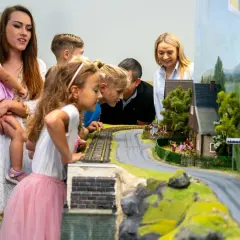 Rodzina podziwia makietę kolejową w parku rozrywki Jelenia Góra. Dzieci zafascynowane pociągiem i domkami.