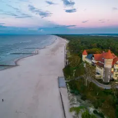 Zachód słońca nad jeziorem Łebsko i plażą. W oddali widać zalesione wybrzeże i malowniczy budynek z wieżą.