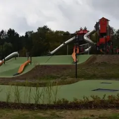 Nowoczesny lunapark w Łodzi z wieloma zjeżdżalniami, wieżami i trampolinami wbudowanymi w zielone wzgórza.