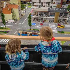 Dwie dziewczynki oglądają miniaturową ulicę z tramwajem i budynkami w parku miniatur Wrocław.