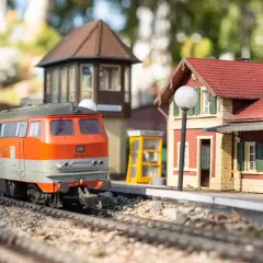 Miniaturowy pociąg na torach w parku miniatur i kolejek dziwnów. Stacja z budynkiem i budką telefoniczną.