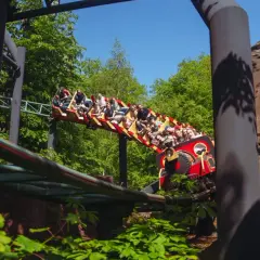 Pasażerowie na kolejce górskiej w kopenhaga park rozrywki, jadący przez zielony las.