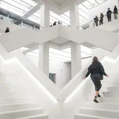 W nowoczesnym, białym wnętrzu nowego muzeum w Warszawie, ludzie wchodzą po schodach.