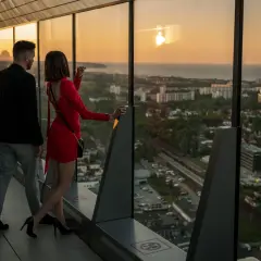 Para spaceruje po tarasie widokowym Olivia Star, podziwiając zachód słońca nad miastem i morzem.