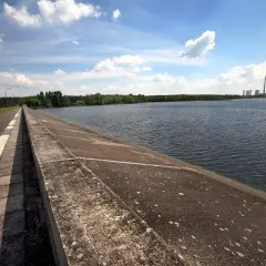 Droga biegnie wzdłuż betonowego muru nad spokojnym zalewem rybnickim. W oddali widać elektrownię.