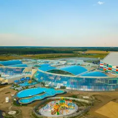 Największy aquapark w Polsce z błękitnymi dachami i kolorowym budynkiem. Widać baseny i plac zabaw.