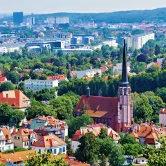 Widok z punkt widokowy Gdańsk: czerwona ceglana katedra z wysoką wieżą, otoczona zielenią i dachami domów. W tle nowoczesne budynki.