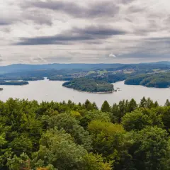 Widok na jezioro solińskie otoczone zielonymi wzgórzami i lasami pod pochmurnym niebem.
