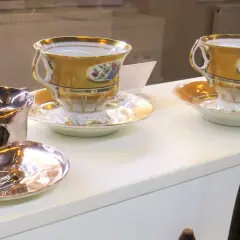 Złote filiżanki z kwiatowymi zdobieniami i srebrny kielich, eksponaty w muzeum czekolady Praga.