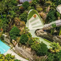 Ekscytująca zjeżdżalnia w Siam Park, z osobą na pontonie wpadającą do basenu. Wokół bujna roślinność.