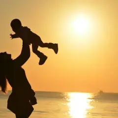 Mama rzuca dziecko w powietrze na tle zachodzącego słońca. Wspaniałe wspomnienia z wakacji w parku rozrywki Mielno.