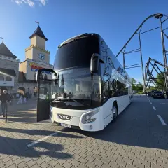 Biały autokar czeka na pasażerów przed wejściem do Energylandii. W tle widać zamek i kolejkę górską. To idealny pociąg do Energylandii!