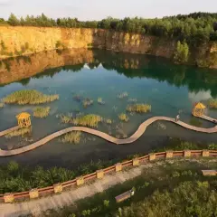 Malowniczy park Gródek z drewnianymi kładkami wijącymi się pośród turkusowej wody i wysepek z trzcinami.
