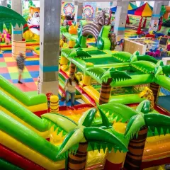 Kolorowy park rozrywki we Wrocławiu z dmuchanymi zjeżdżalniami i palmami. Dzieci biegają po kolorowej macie.