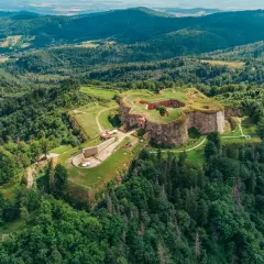 Forteca na wzgórzu, otoczona lasem, niczym srebrna góra w zieleni.