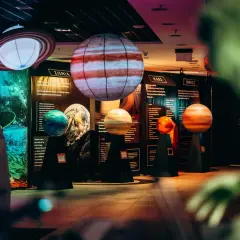 Modele planet i pierścieni Saturna w kosmo parku. W tle tablice informacyjne o Ziemi, Marsie i Jowiszu.