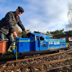 Mężczyzna w czapce i kurtce obsługuje niebieską lokomotywę PKP SM42, która jest częścią kolejki. Obok wagon towarowy.