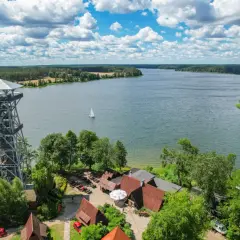 Wieża widokowa i zabudowania nad jeziorem, idealne kaszubskie atrakcje. Żaglówka na wodzie, las i błękitne niebo.