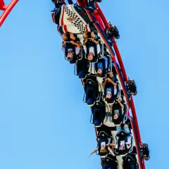 Ludzie wiszą do góry nogami na kolejce górskiej, która pędzi po czerwonej konstrukcji. To prawdziwa formuła adrenaliny!
