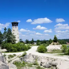 Kamienna wieża widokowa Józefów góruje nad piaszczystym krajobrazem, otoczona zielenią i błękitnym niebem z chmurami.
