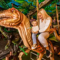 Uśmiechnięta mama z dzieckiem na dinozaurze w góraszka park rozrywki. Wesoła przejażdżka wśród prehistorycznych stworzeń.