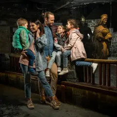 Rodzina zwiedza kopalnię soli w Wieliczce. Dzieci z rodzicami podziwiają solne rzeźby królów i rycerzy.