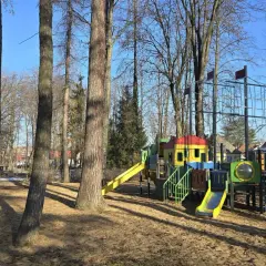 Kolorowy plac zabaw w parku rozrywki Nowy Sącz, z drabinkami, zjeżdżalniami i siatką do wspinaczki, otoczony drzewami.