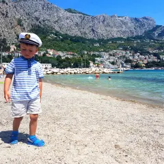 Chłopiec w kapitańskim kapeluszu na plaży w Chorwacji. W tle góry i miasteczko. Idealne miejsce na wakacje, jak w parku rozrywki Chorwacja.