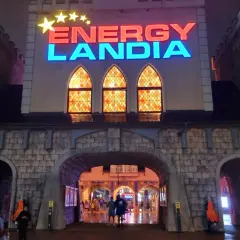 Wejście do Energylandii nocą, mimo deszczu, widać ludzi wchodzących pod łukiem.