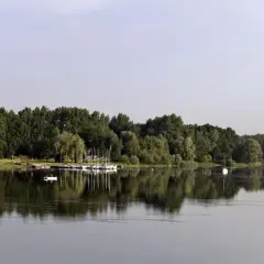 Spokojne jezioro Przeczyckie z odbijającymi się w wodzie drzewami i żaglówkami. Na wodzie widać samotną łódkę.