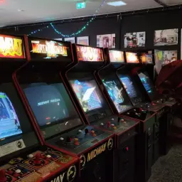 Rząd klasycznych automatów do gier, w tym Mortal Kombat, w sali gier.