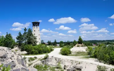 Kamienna wieża widokowa Józefów góruje nad piaszczystym krajobrazem, otoczona zielenią i błękitnym niebem z chmurami.