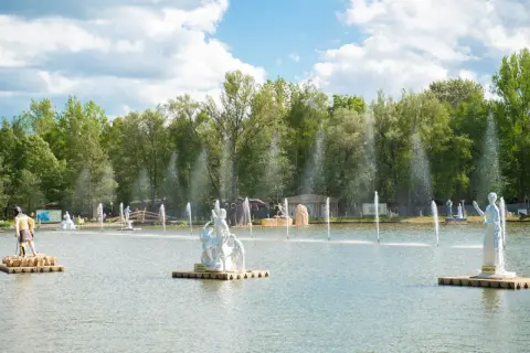 Park mitologii na wodzie z rzeźbami bogów i bogiń, otoczony zielenią i fontannami.