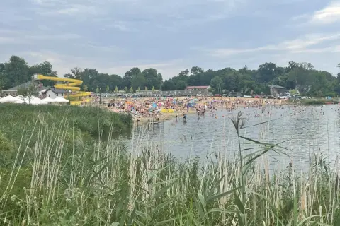 Tłum ludzi wypoczywa nad wodą na plaży w Lisowicach. W oddali widać żółtą zjeżdżalnię wodną.