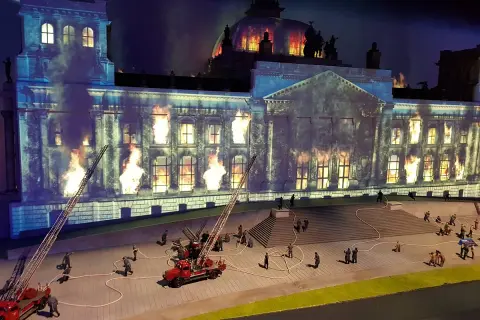Miniaturowy pożar Reichstagu w **little big city Berlin**. Strażacy walczą z płomieniami, a dym unosi się w mroku.