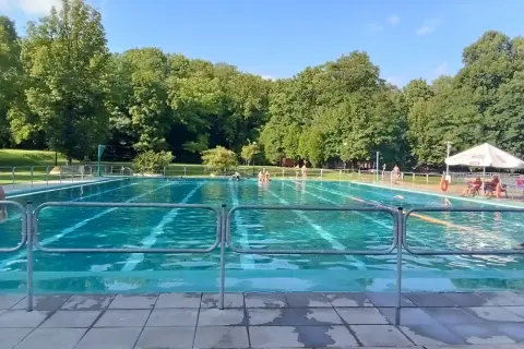 Słoneczny dzień nad basenem w Bytomiu. Woda kusi chłodem, a wokół zielone drzewa.