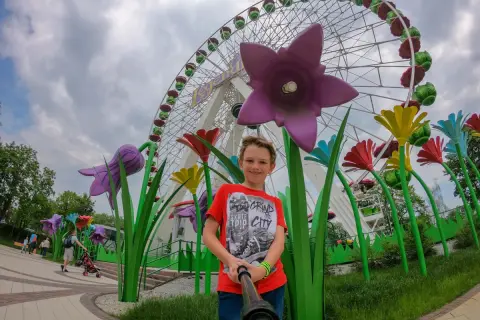 Chłopiec pozuje do selfie na tle diabelskiego młyna w chorzowskim wesołym miasteczku, otoczony kolorowymi, gigantycznymi kwiatami.