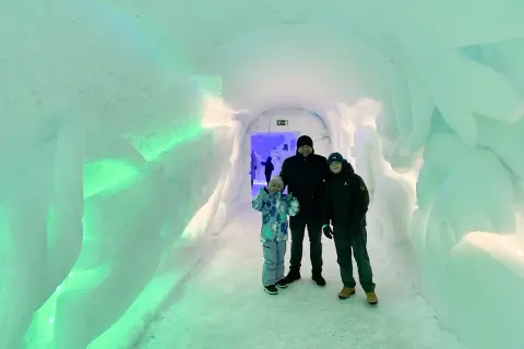 Rodzina w lodowym tunelu, gdzieś w okolicy wioski Mikołaja w Finlandii. Ściany lśnią zielonym światłem.