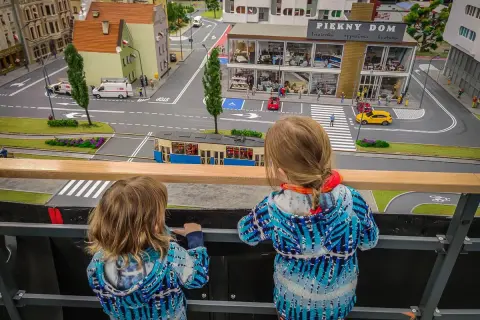 Dwie dziewczynki oglądają miniaturową ulicę z tramwajem i budynkami w parku miniatur Wrocław.
