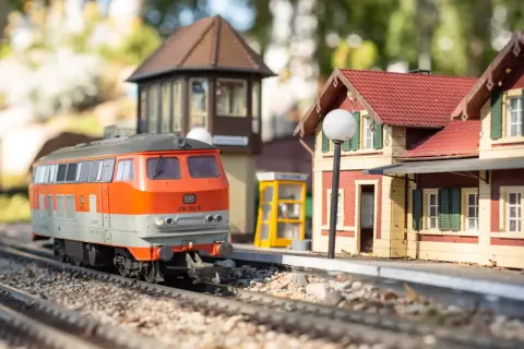 Miniaturowy pociąg na torach w parku miniatur i kolejek dziwnów. Stacja z budynkiem i budką telefoniczną.