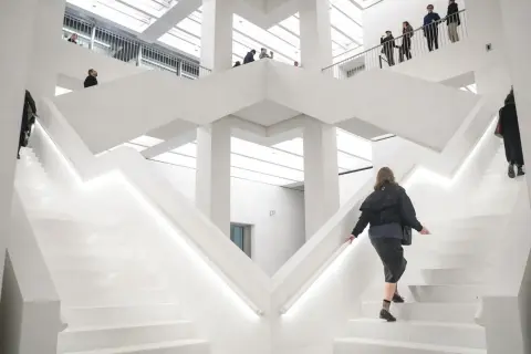 W nowoczesnym, białym wnętrzu nowego muzeum w Warszawie, ludzie wchodzą po schodach.