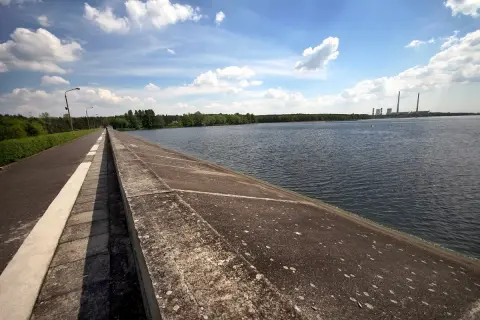 Droga biegnie wzdłuż betonowego muru nad spokojnym zalewem rybnickim. W oddali widać elektrownię.
