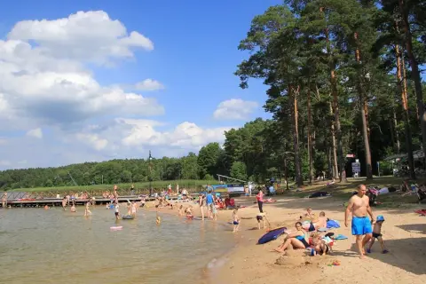 Słoneczna augustowska plaża tętni życiem. Ludzie kąpią się, opalają i relaksują na piasku, ciesząc się letnim dniem nad jeziorem.