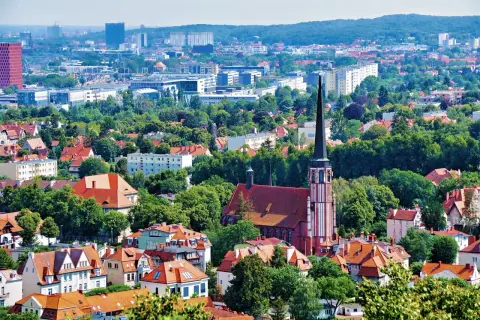 Widok z punkt widokowy Gdańsk: czerwona ceglana katedra z wysoką wieżą, otoczona zielenią i dachami domów. W tle nowoczesne budynki.